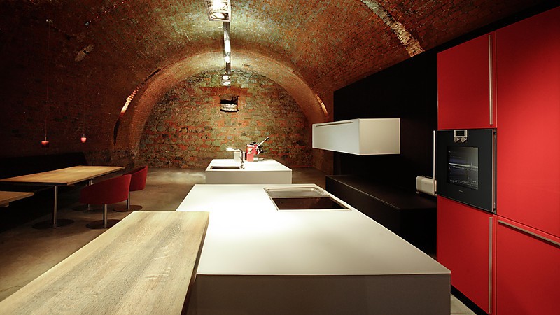 Hochwertige Ausstellungsküche mit modernen Design und hochwertigen Materialien. Hochschränke in Rot. Sidebord in Schwarz. Weiße Kücheninsel.